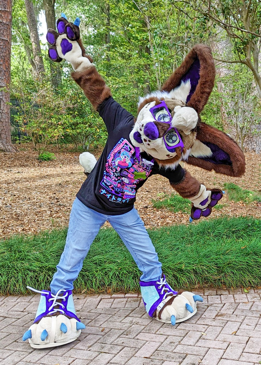 Jordan is fursuiting in a public nature park as their partial and she is standing on a path bending over with her arms wide open.